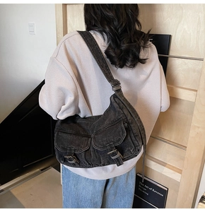 Detail of vintage black denim biker shoulder bag with dual utility buckle pockets on model