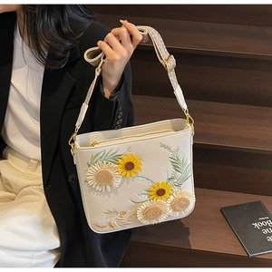 Detail of sunflower and daisy embroidery on a white leather bag with a woven strap