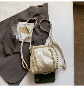 Close-up of cream quilted bucket bag with gold chain and drawstring on a stylish background