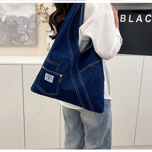 Close-up of deep blue washed denim tote bag with diagonal stitching and a patch pocket