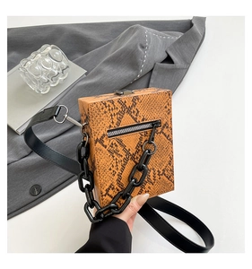 Detail view of orange-brown snakeskin square bag with dual strap and metal lock