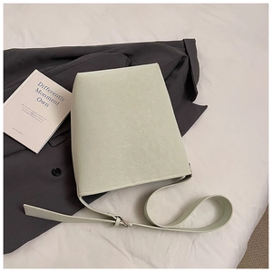 Detailaufnahme der salbeigrünen Beuteltasche mit Lederstruktur auf grauem Anzug und Laken