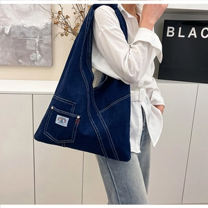Detail view of deep blue denim tote bag with visible white stitching and logo patch
