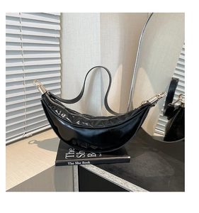 Close-up of black glossy patent leather crescent bag with elegant gold hardware rings