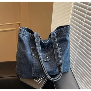 Detail of blue washed denim tote bag showing the front flap pocket and silver metal button