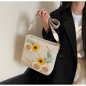 Detail of cream crossbody bag featuring floral sunflower embroidery and a woven strap