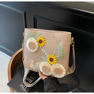Detail of floral embroidery on beige crossbody bag with patterned shoulder strap
