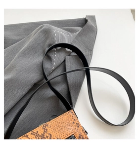 Detailed macro view of an orange faux snakeskin crossbody bag with a black leather strap
