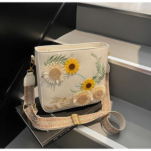 Detail of sunflower embroidery on white faux leather crossbody bag with wide strap