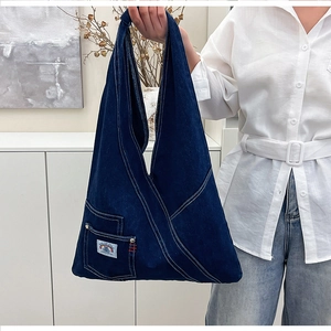 Detailed view of dark blue denim shoulder bag with white stitching and stylish logo patch