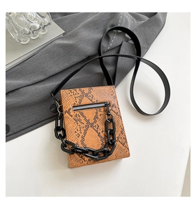 Detail of yellow-brown snakeskin texture crossbody bag with black acrylic chain handle