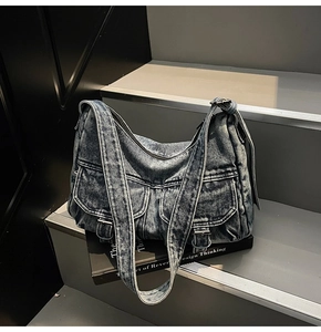 Detail of dark washed denim shoulder bag with vintage metal buckles and utility pockets