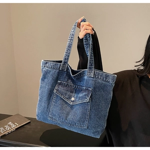 Detail of blue denim tote bag featuring a front pocket with metal button and textured fabric
