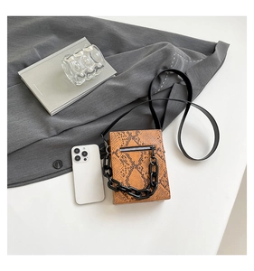 Detail of crossbody phone bag with orange snakeskin texture and thick black resin chain