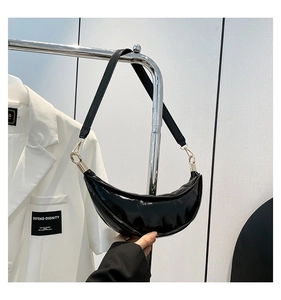 Detail of glossy black patent leather crescent bag with gold metal hardware and strap