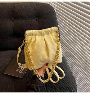Detail of light beige quilted bucket bag featuring drawstring and gold chain strap
