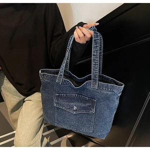 Detail of dark blue denim tote bag featuring front flap pocket with silver metal buckle