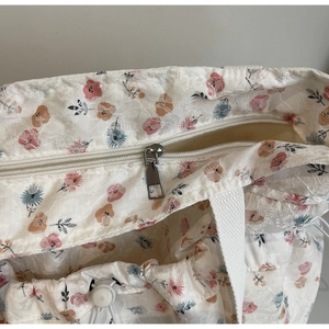 Detail view of the floral lace texture with metal zipper and drawstring on a white tote bag