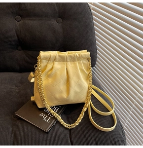 Close-up of quilted chain bag with ruched design on black corduroy surface