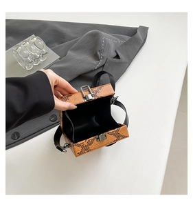 Detail view of snakeskin pattern leather handbag with silver clasp and black wide strap
