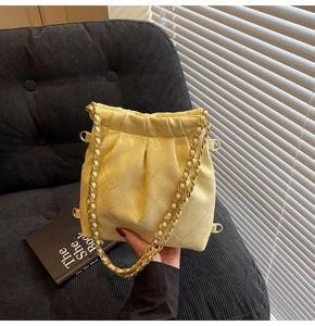 Detail of quilted leather drawstring bucket bag in cream yellow with gold chain strap
