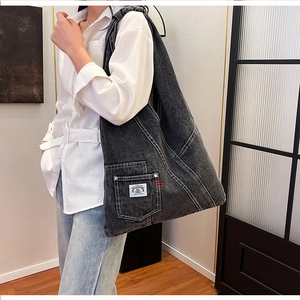 Detail of grey washed denim hobo bag featuring contrast white stitching and textile label