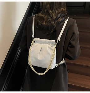 Detail of light gray quilted mini backpack with decorative gold chain on a model