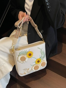 White crossbody bag with floral embroidery and wide ethnic strap shown on a model