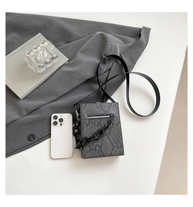 Detail view of grey snake-print crossbody bag with matte black chain and phone storage