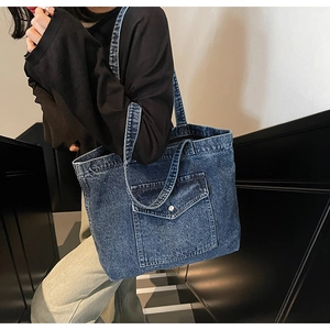 Detail view of durable blue denim tote bag featuring a front pocket with metal button