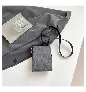 Detail of gray snakeskin texture on a rectangular crossbody bag with a black leather strap