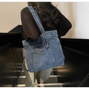 Detail of blue denim tote bag featuring a front pocket with metallic button closure