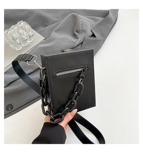 Close-up of black textured box crossbody bag with chunky plastic chain and silver hardware