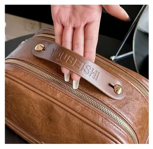 Close-up of brown textured leather cosmetic bag with embossed handle and gold rivets