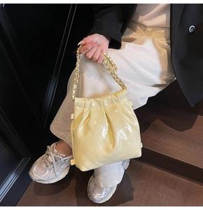 Detail of light yellow quilted bucket bag with gold chain strap and glossy finish