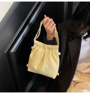Detail view of yellow quilted chain bag showing glossy finish and gathered closure