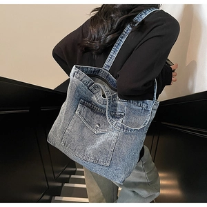 Detail of vintage blue denim tote bag with a front flap pocket and silver metal button