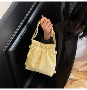 Detail of light yellow bucket bag featuring quilted diamond pattern and chain strap