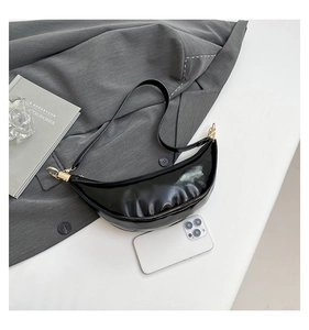 Detail of glossy black patent leather dumpling bag with gold zipper and mobile size reference