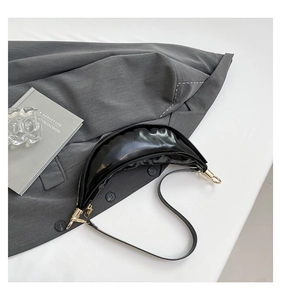Detail of glossy black crescent shoulder bag with golden hardware on a white background