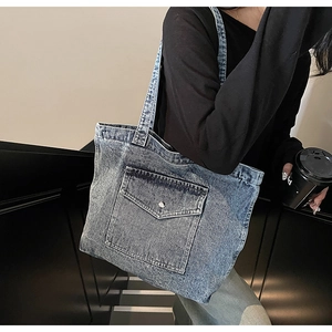Detail of light blue washed denim tote bag with metal buckle pocket worn by a model