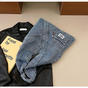 Detail of blue washed denim bag with pocket stitching lying on a black leather jacket
