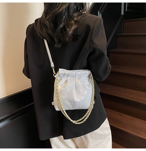 Detail of grey quilted bucket bag with chain strap shown on a model in urban setting