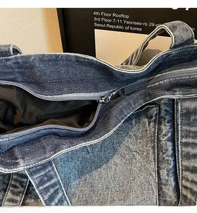Detail view of the smooth metal zipper closure and denim fabric texture on the tote bag