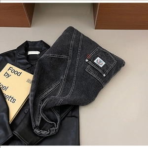 Detail of black denim messenger bag featuring white stitching and side pocket with colorful logo
