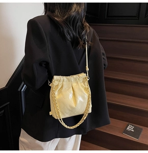 Close-up of a quilted bucket bag in pale yellow with a gold chain strap on a model