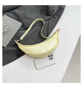 Detail view of a pale yellow crescent bag with gold zippers next to a smartphone