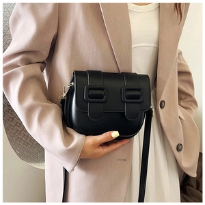 Détail d'un sac besace noir avec doubles boucles porté par un mannequin en costume rose