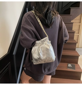 Close-up of silver quilted bucket bag with golden chain strap on a model shoulder