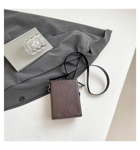 Macro detail of brown snake-patterned leather mini box bag with slim black shoulder strap